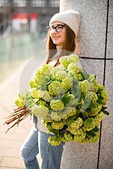 Smiling girl with brown hair in a knitted sweater and hat with a bouquet of flowers