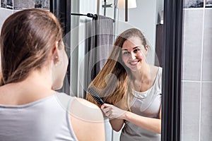 Smiling girl brushing her long hair in front of mirror