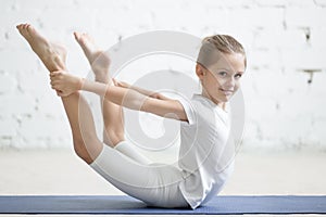 Smiling girl child in dhanurasana pose, white studio background