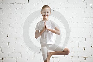 Smiling girl child in Vrksasana pose, white studio background