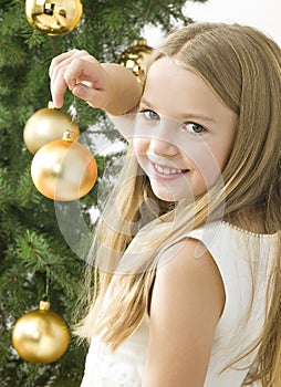 Smiling girl with christmas balls next to green tr