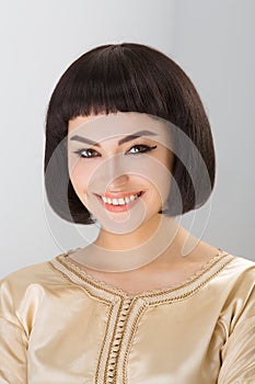 Smiling girl with Cleopatra's make-up and haircut posing in studio