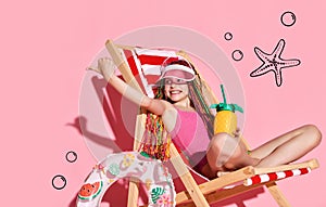 Smiling girl with colorful hair in swimsuit and sun cap relaxing on sunbed with pineapple and showing thumb sign with finger