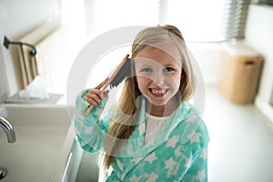 Smiling girl combing her hair in bathroom