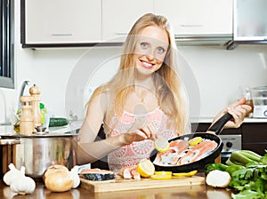 Smiling girl cooking salmon fish with lemon