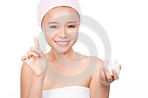 Smiling girl in a cream on her finger, holding a box of cosmetic cream looking at the camera