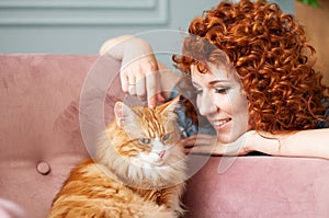 Smiling girl with curly red hair caresses a red cat