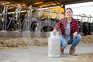 Smiling girl dairy farm worker posing with milk can in cowshed