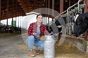 Smiling girl dairy farm worker posing with milk can in cowshed