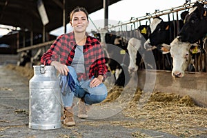 Smiling girl dairy farm worker posing with milk can in cowshed