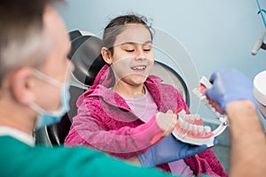 Smiling girl in dentist chair educating about proper tooth-brushing by her pediatric dentist