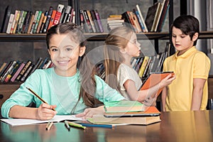 Smiling girl doing homework with classmates talking behind