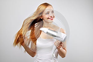 Smiling girl drying her hair with a blow dryer