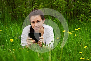 Smiling girl with ebook lying on the grass