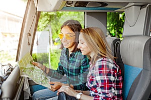 Smiling girl friends with map traveling by tour in bus