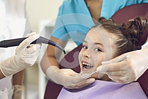 Smiling girl getting tooth curing with luminous dental filling from dentist