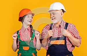 smiling girl and grandfather builder in helmet on yellow background
