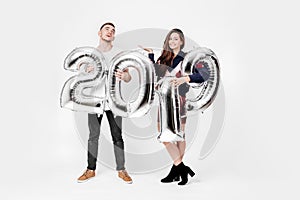 Smiling girl and guy dressed in a stylish clothes are having fun with balloons in the shape of numbers 2019 on a white