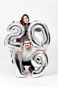 Smiling girl and guy dressed in a stylish clothes are having fun with balloons in the shape of numbers 2019 on a white