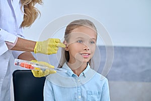 Smiling girl and hands of otolaryngologist near ear