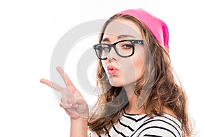 Smiling girl in hat and glasses showing two fingers and pouting