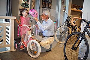 Smiling girl and her grandfather buying bicycle and helmets in bike shop