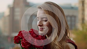 Smiling girl holding bunch outdoors. Cheerful woman smelling flowers on street.