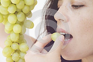 Smiling girl holding grapes near her face and smiling broadly to the viewer