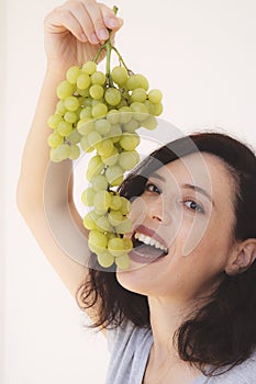 Smiling girl holding grapes near her face and smiling broadly to the viewer
