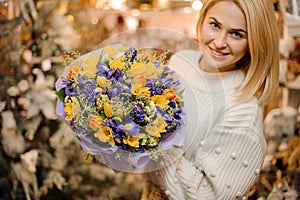 Smiling girl holding a little bouquet with purple and white flowers wrapped in gift paper