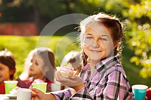 Smiling girl holds cupcake with her friends behind