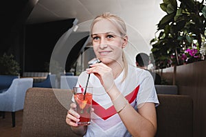 Smiling girl holds a glass and drinks a red drink