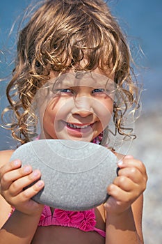 Smiling girl holds in hands pebble on seacoast