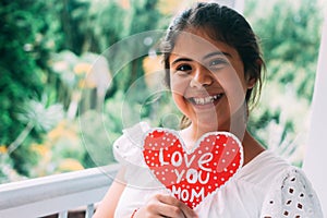 Smiling girl with an I love you mom sign. Concept of love. Happy mother`s day. portrait of beautiful girl with out of focus natur