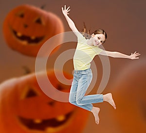 Smiling girl jumping over pumpkins background