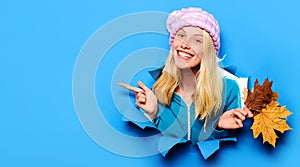 Smiling girl in knitted hat with yellow leavas looking through paper hole pointing at copy space.