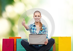 Smiling girl with laptop comuter and shopping bags