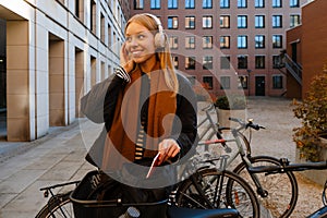 Smiling girl listening music with headphones while standing with bike outdoors