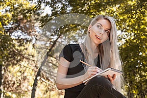 Smiling girl with a long silver hairs drawing on notebook in the park