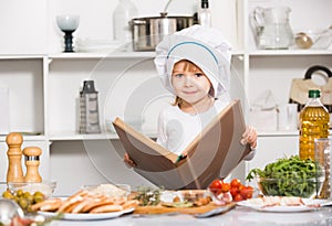 Smiling girl is looking new recipe in big book in the kitchen