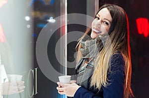 Smiling girl looking at the shop window before entering. Woman oon the festive Christmas market at night