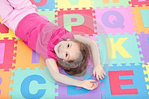 Smiling girl lying on alphabet tiles