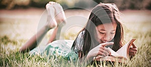 Smiling girl lying on grass and reading book in park