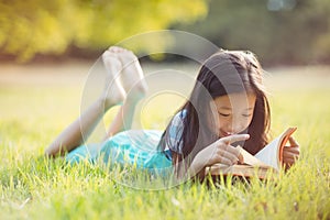 Smiling girl lying on grass and reading book in park