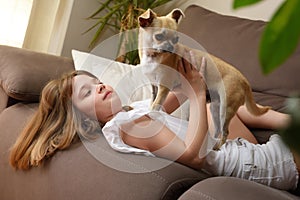 Smiling girl lying with her dog on the sofa playing