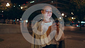 Smiling girl messaging cellphone on evening street close up. Short hair woman