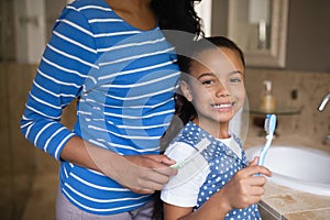 Smiling girl with mother brushing teeth in bathroom