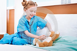 Smiling girl nurse listening teddy bear`s heartbeat with stethoscope