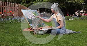 Smiling girl painting on canvas with water colors in the garden