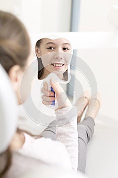 Smiling girl patient looking at mirror in dental clinic